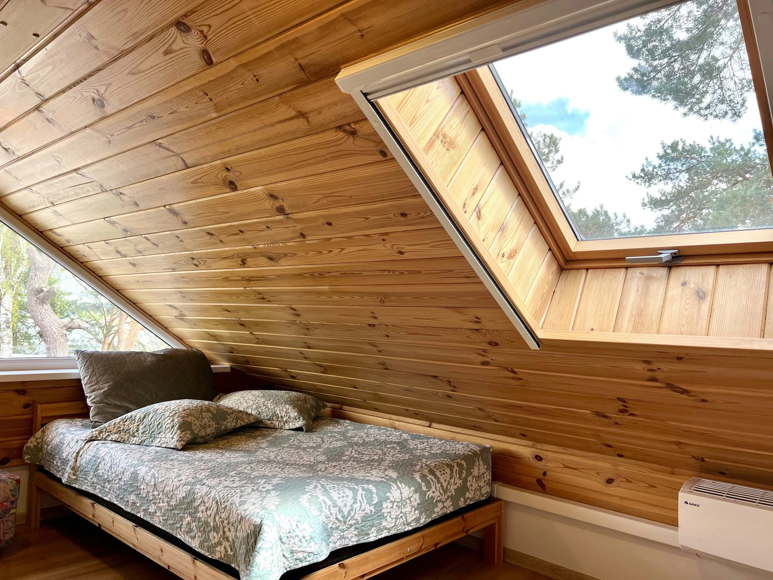 7A kotedžas – Lova medinėje palėpėje po stoglangiu, pro kurį matyti medžių lajos