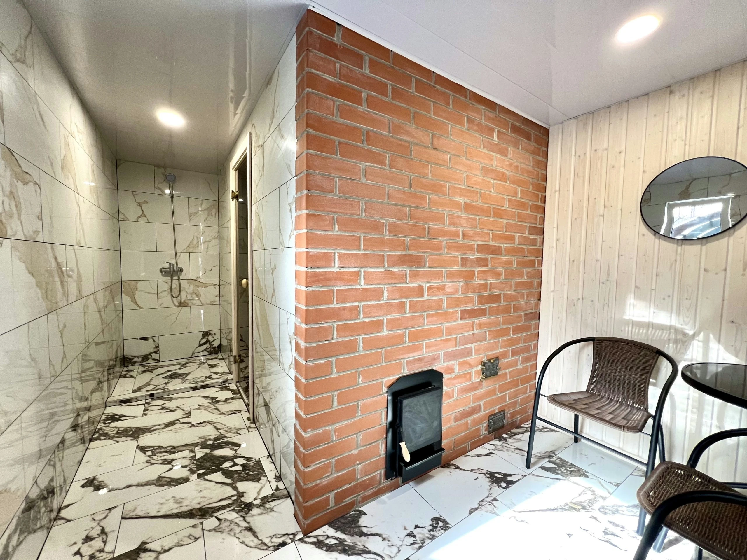 4 namelis – Dušo erdvė ir raudonų plytų siena su krosnies durelėmis šalia krėslų