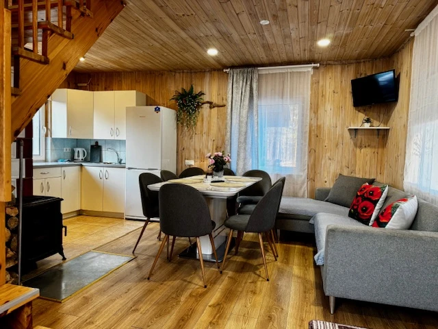 2 namelis – Bendra virtuvės ir svetainės erdvė su valgomojo stalu bei pilka sofa.
