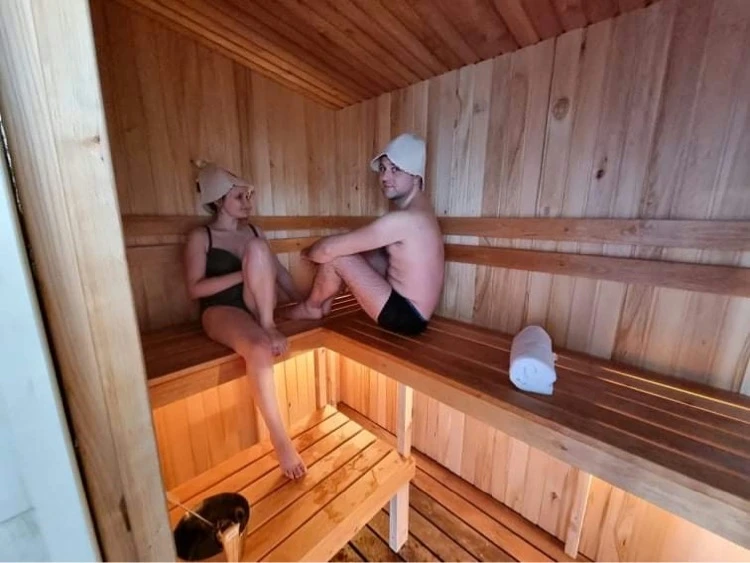 10 namelis – Žmonės su pirties kepurėmis sėdi ant medinių suolų medinėmis sienomis apkaltoje pirtyje