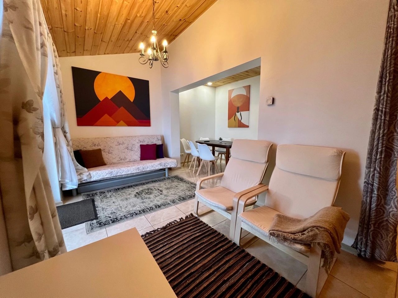 7A kotedžas – Šviesūs krėslai ir sofa po spalvingu paveikslu, ant grindų raštuoti kilimai