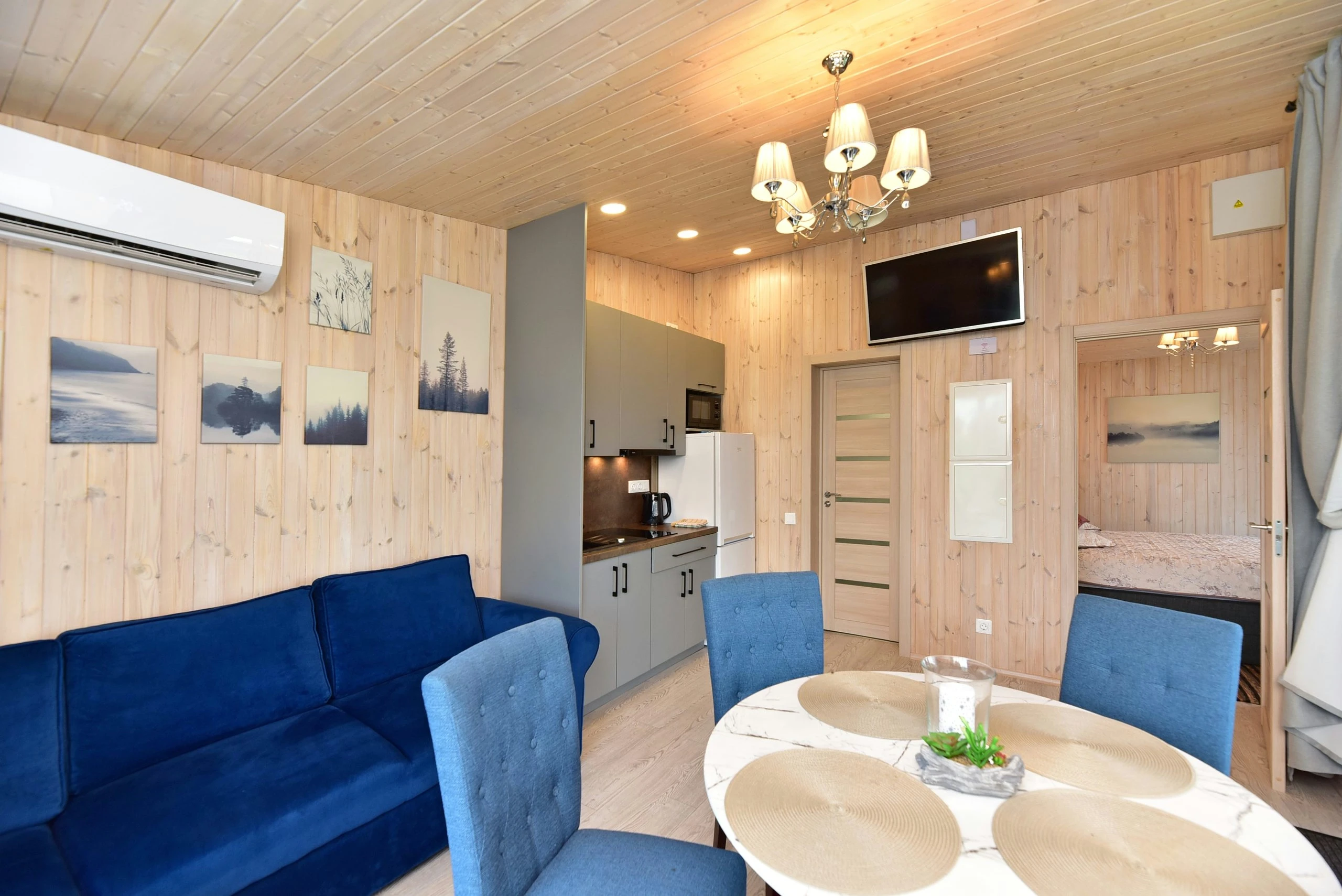 10 namelis – Svetainės ir virtuvės erdvė su mėlyna sofa, mėlynomis valgomojo kėdėmis ir apvaliu stalu