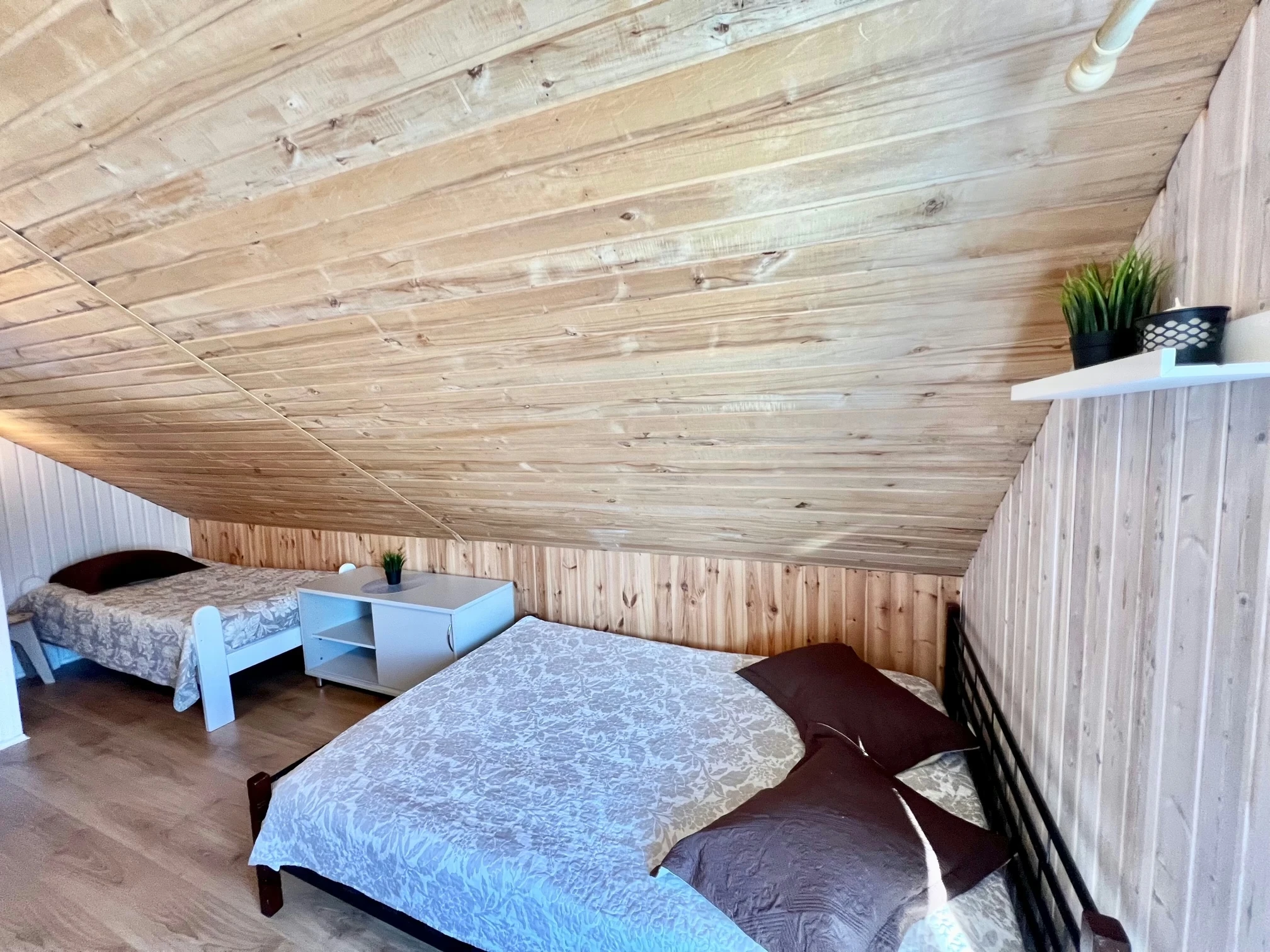 2 namelis – Mansardos miegamasis su lovomis po žemomis medinėmis lubomis ir lentyna pertvaroje.
