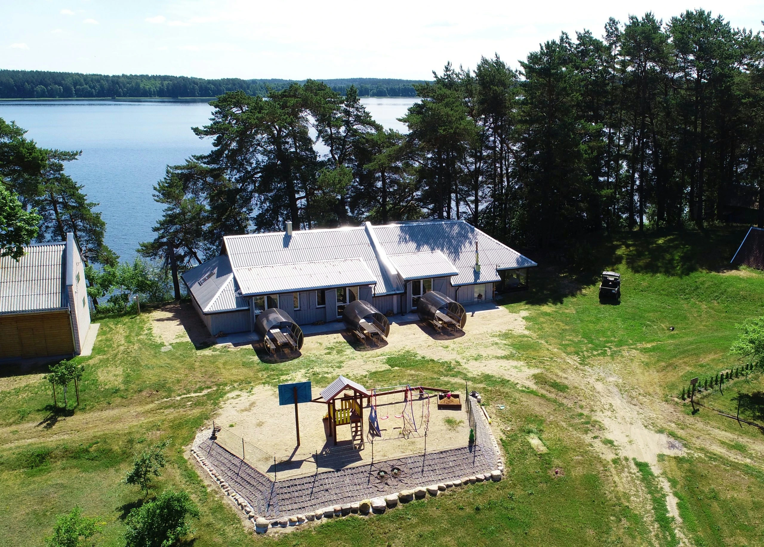 7A kotedžas – Namelio, žaidimų aikštelės ir medžiais apaugusio ežero kranto panorama iš oro
