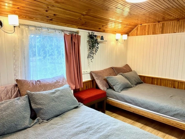 6 namelis – Pilkomis lovatiesėmis užklotos lovos prie lango su rausvomis užuolaidomis