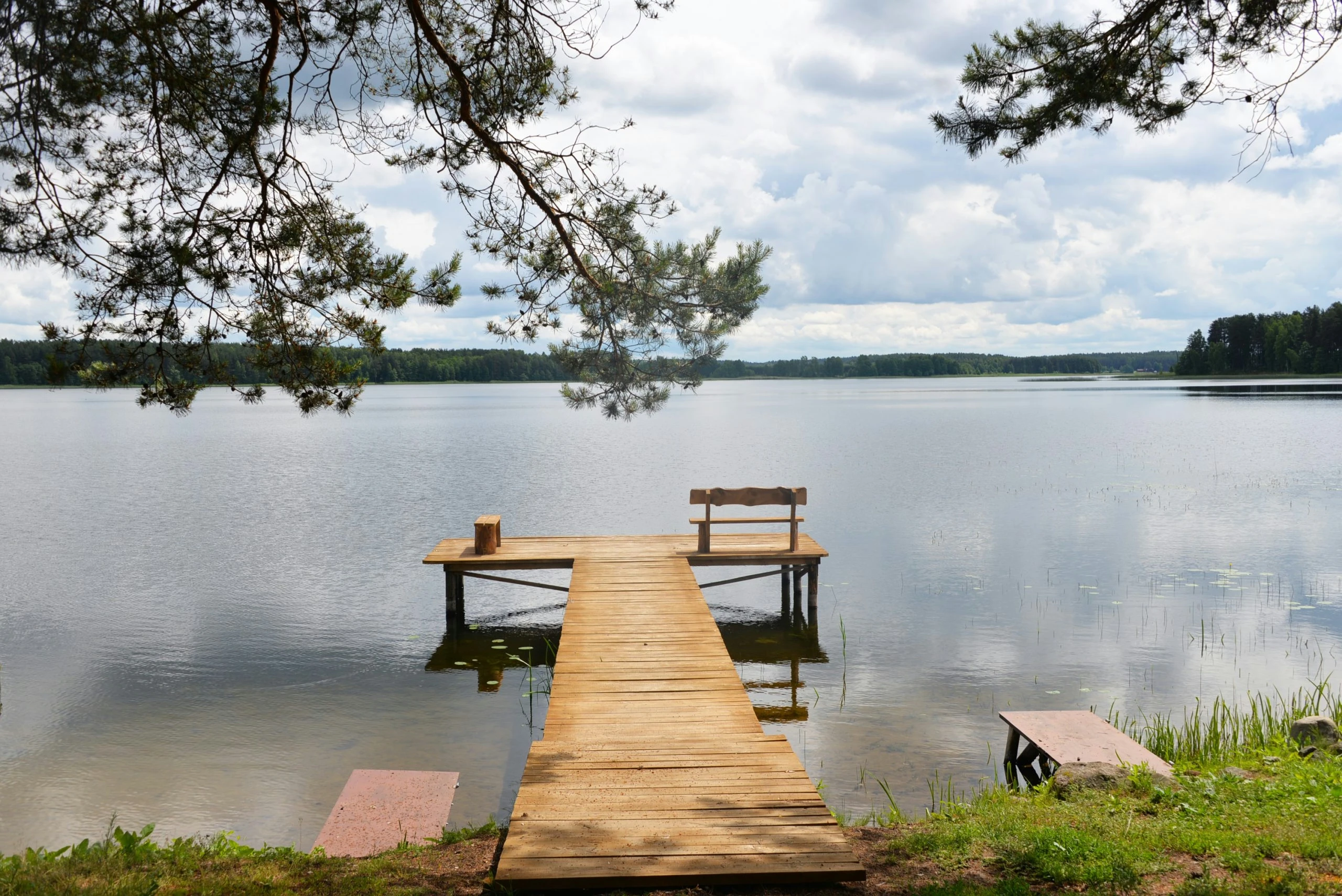 4 namelis – Ilgas medinis lieptas veda į ramų ežerą, jo gale stovi suolas.