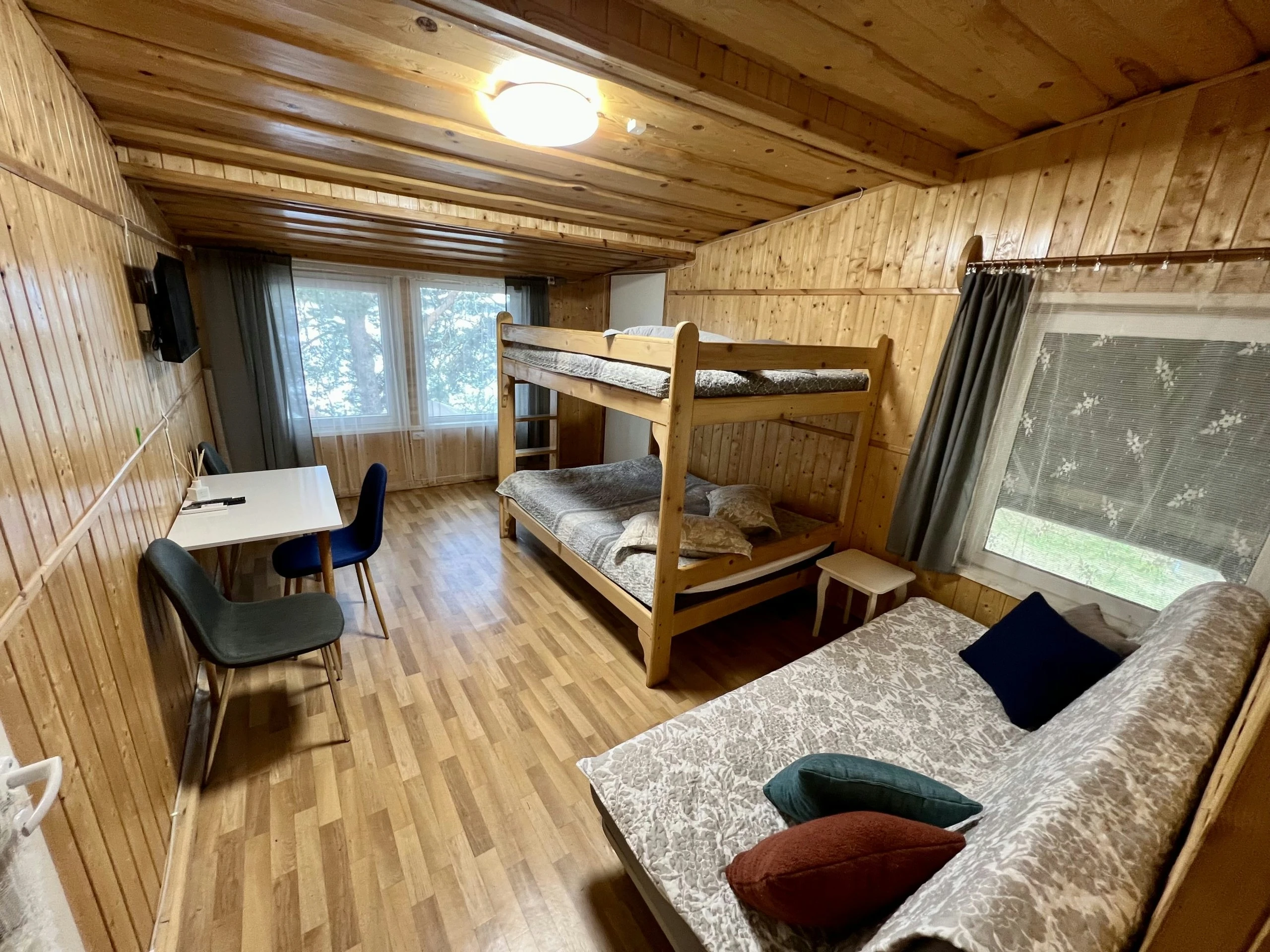 7D kotedžas – Medinis kambarys su dviaukšte lova, sofomis ir stalu prie didelio lango