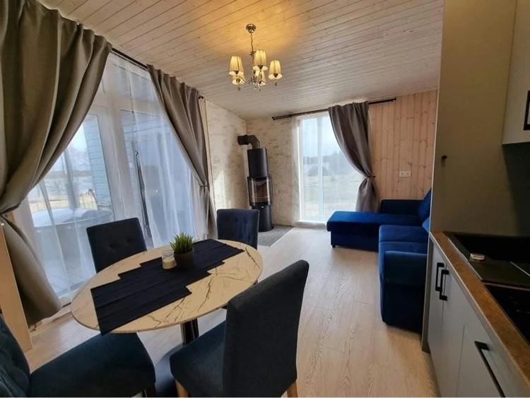10 namelis – Virtuvės ir svetainės vaizdas su apvaliu stalu, mėlyna sofa ir krosnele prie lango