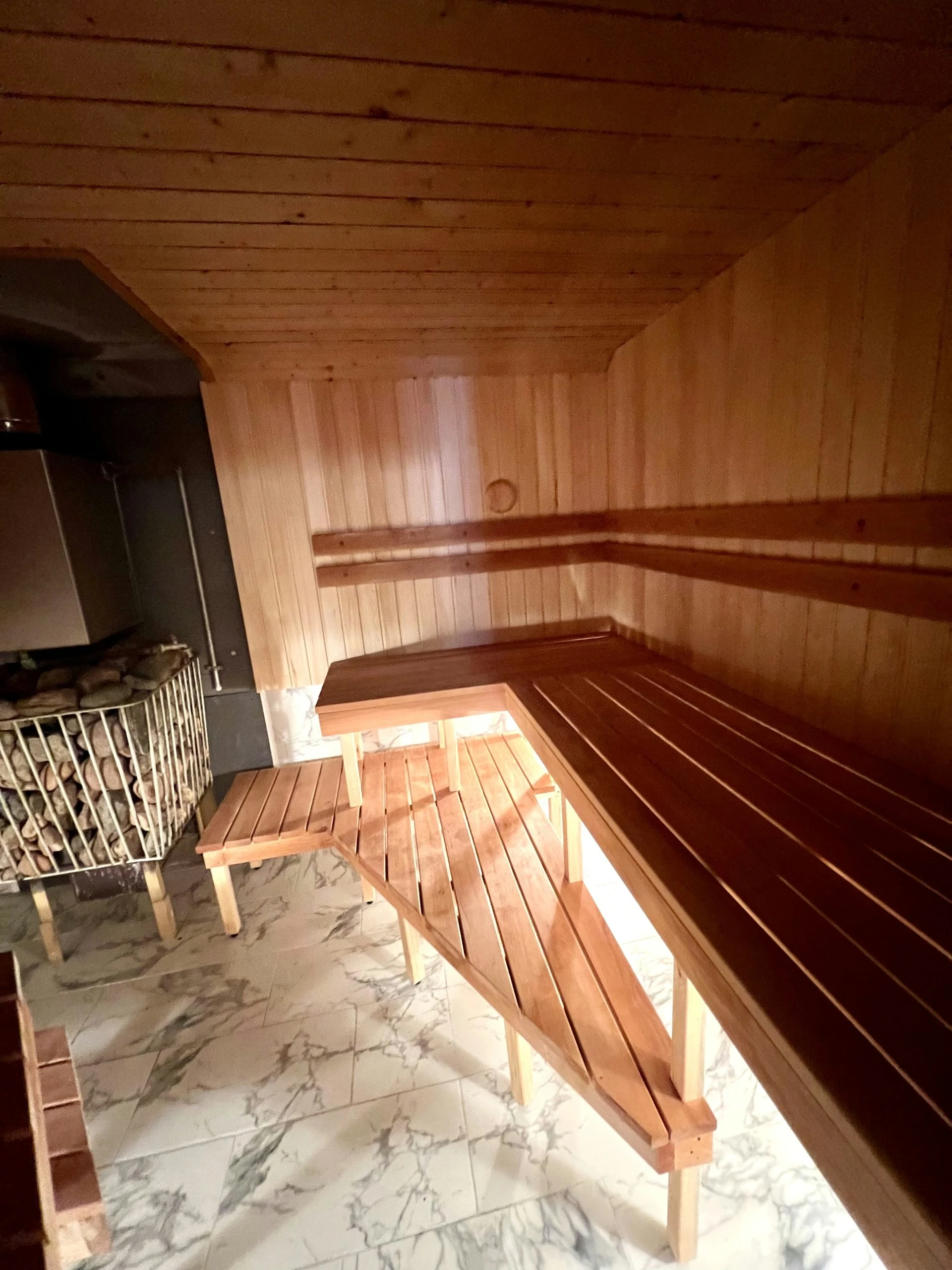 7D kotedžas – Medinės pirties vidus su ilgu suolu palei sieną ir krosnele kampe