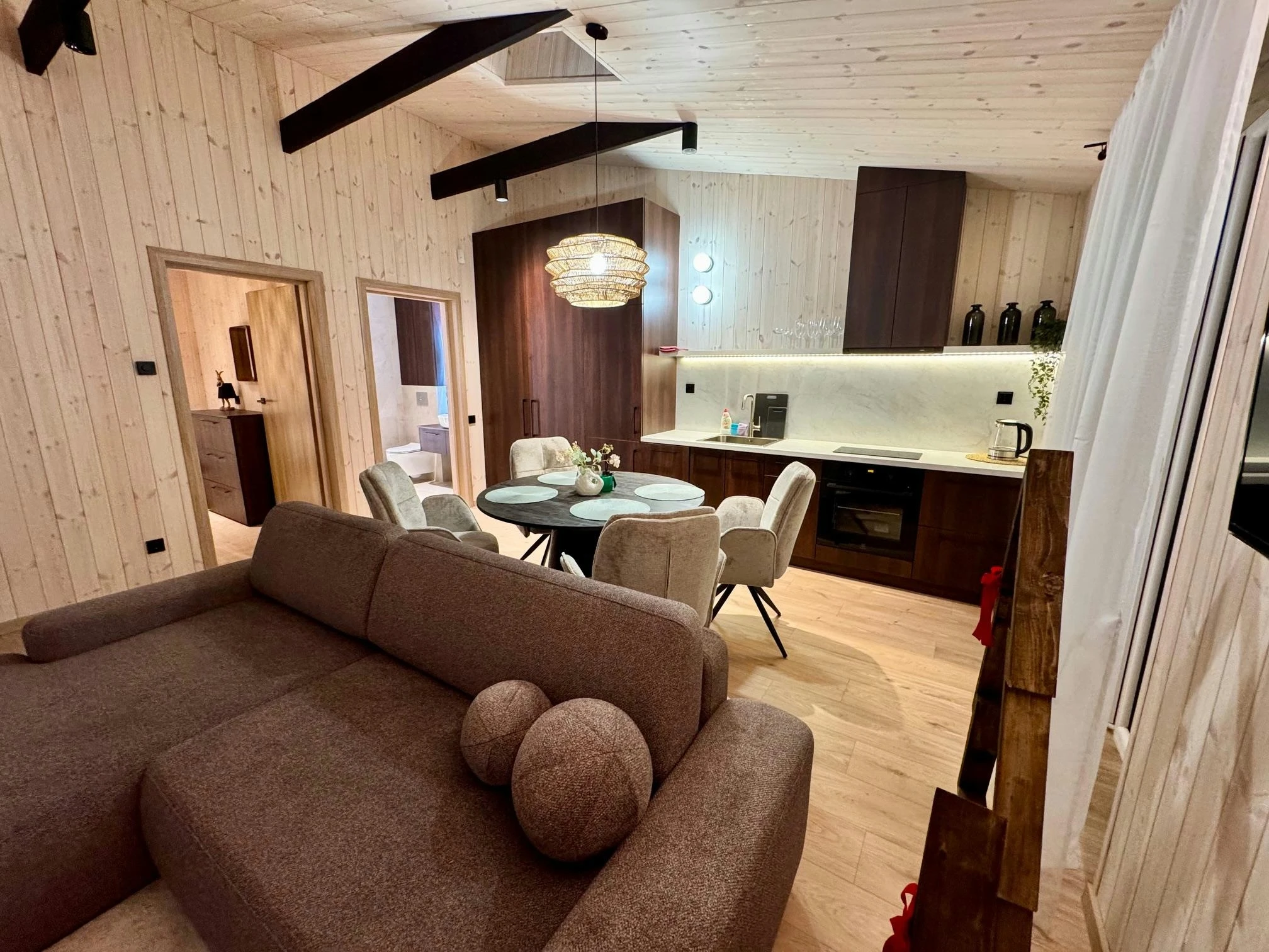 Namelis su baseinu – Svetainė su kampine sofa, apvaliu valgomojo stalu ir atvira virtuve.