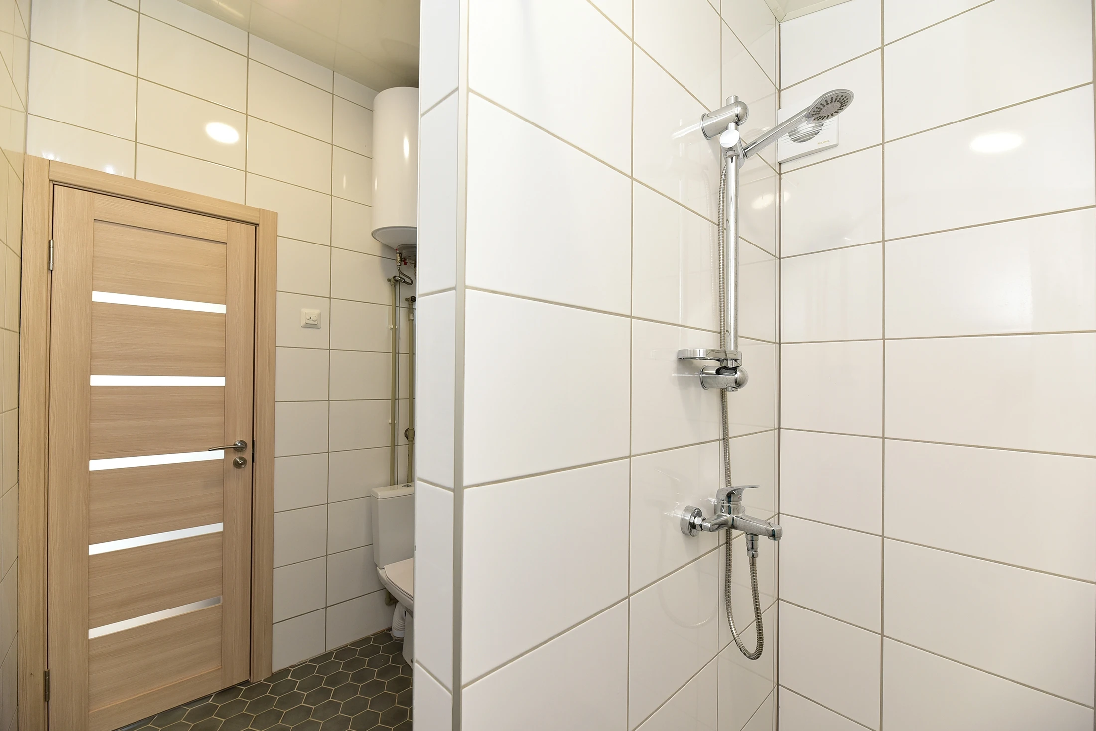 10 namelis – Dušo zona su baltomis stačiakampėmis plytelėmis, dušo galvute ir šviesiomis medinėmis durimis