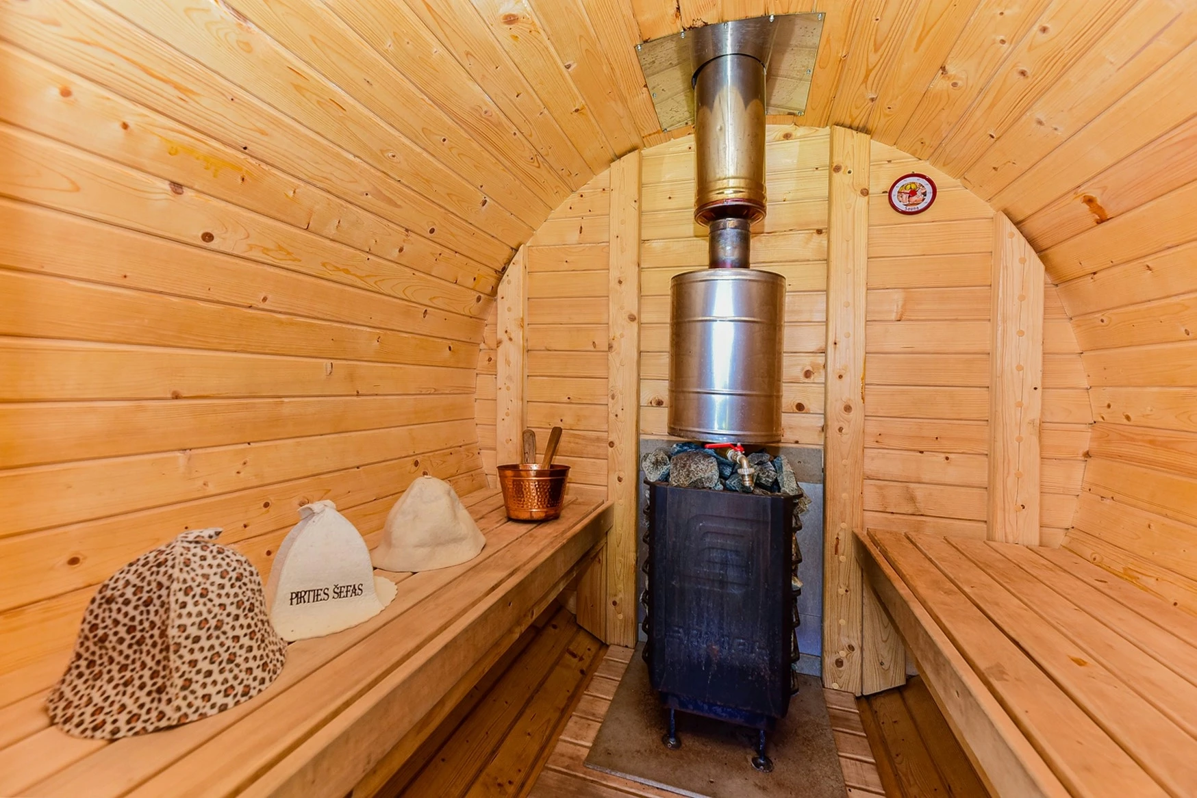 6 namelis – Apvalios medinės pirties vidus su suolais iš abiejų pusių ir krosnele gale