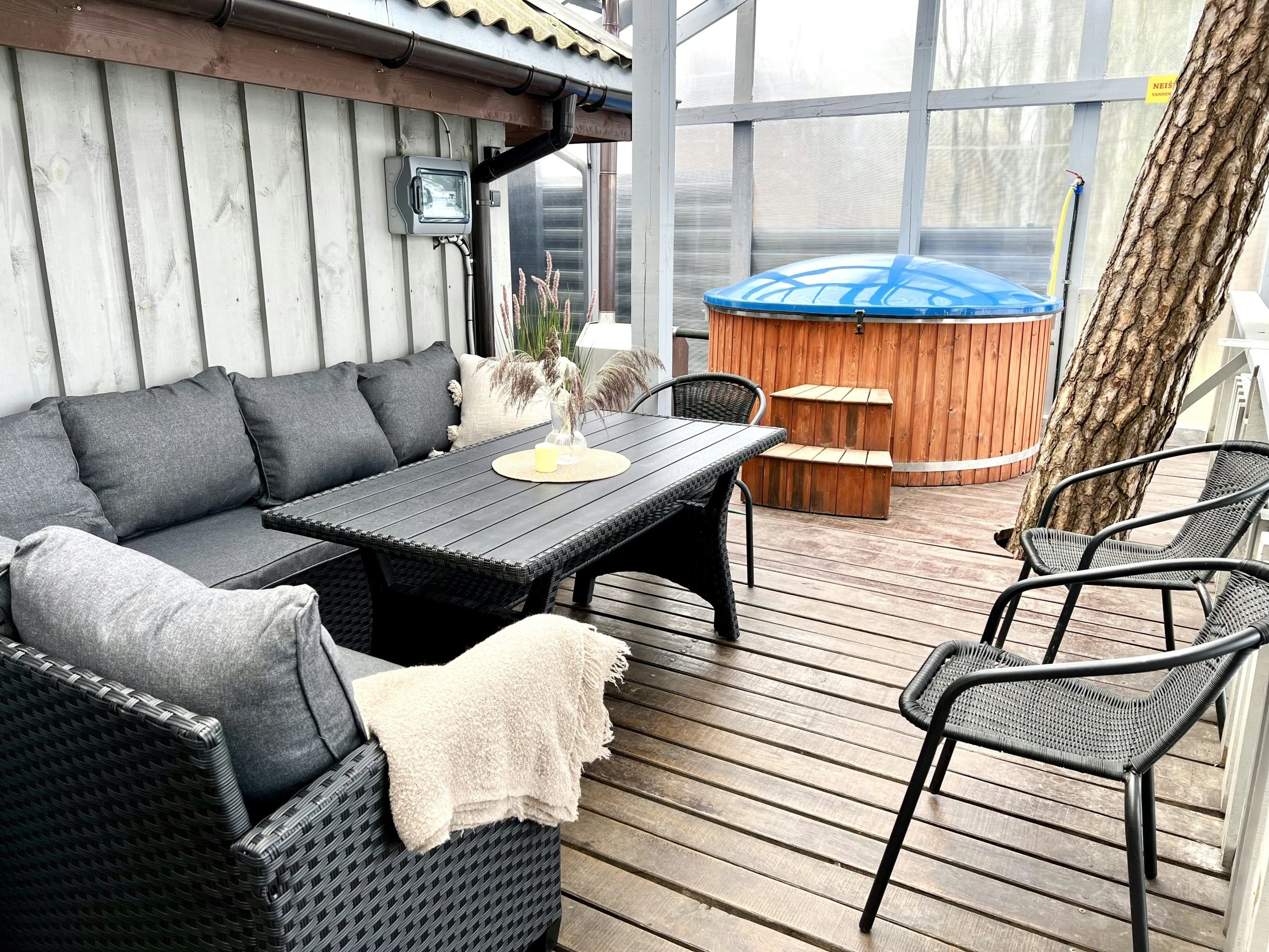 7A kotedžas – Terasos poilsio kampas su pilka sofa, stalu, juodomis kėdėmis ir mėlynai uždengtu kubilu
