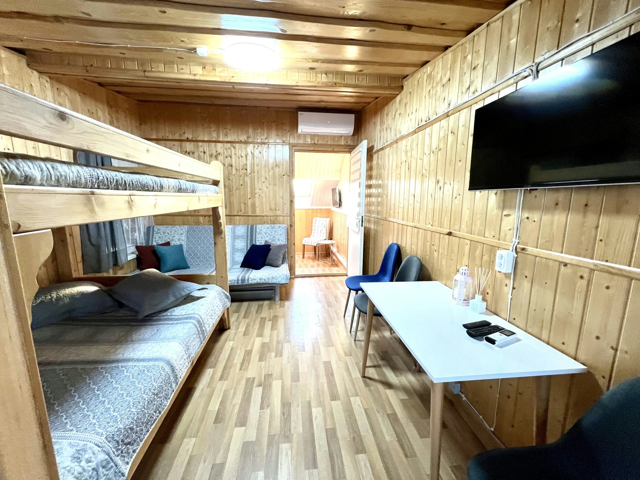 7D kotedžas – Medinis kambarys su dviaukšte lova, sofa, stalu, mėlynomis kėdėmis ir televizoriumi