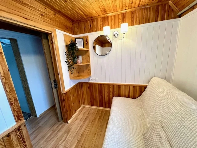 6 namelis – Nedidelė poilsio erdvė su smėlio spalvos sofa, apvaliu veidrodžiu ir medine sienų apdaila